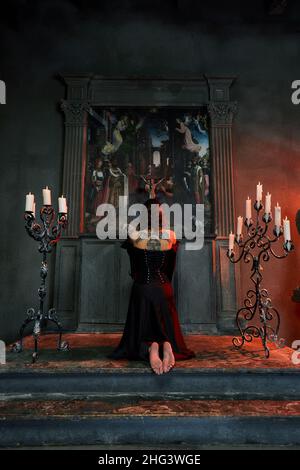 Gebet in der Kirche. Barfuß Frau mit dunklem Haar kniet in der Kirche, zündet eine Kerze an und betet vor der Ikone. Stockfoto