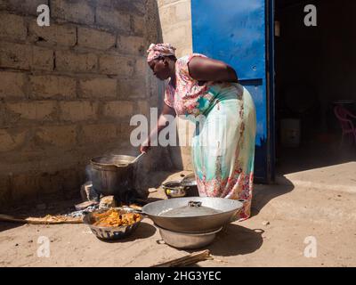 Senegal, Afrika - Jan, 2019: Senegalesische Frau in einer traditionellen Tracht namens 'boubou', die das Essen im afrikanischen Haus kocht. Stockfoto