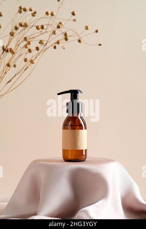 Leere braune Bernstein Glasflasche mit Etikett Mockup und trockenen Blumen auf beigem Hintergrund. Seifenspender, Duschgel, Shampoo-Behälter-Design auf Dais Pod Stockfoto