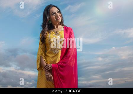 Glückliche Frau in gelbem Salwar, die unter dem blauen Himmel steht Stockfoto