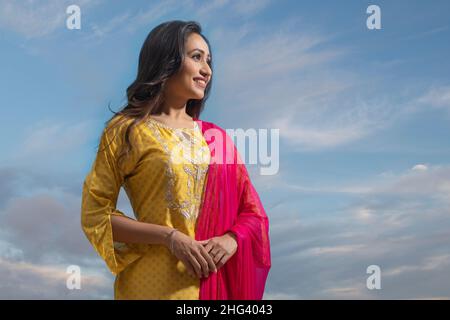 Glückliche Frau in gelbem Salwar, die unter dem blauen Himmel steht Stockfoto