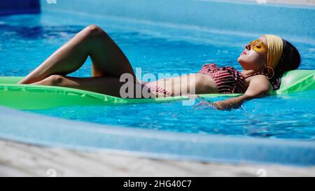 Junge Frau mit Sonnenbrillen schwimmt im Pool Stockfoto