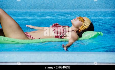 Junge Frau in Sonnenbrillen schwimmend auf aufblasbarer Matratze im Schwimmbad Stockfoto