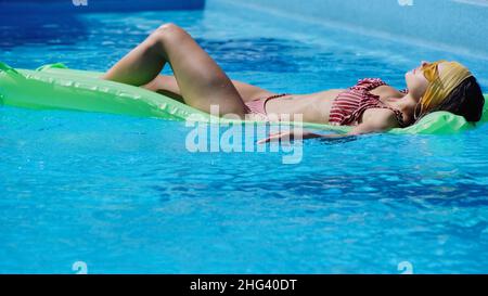 Junge Frau in Sonnenbrillen, die im Schwimmbad auf dem Schwimm-Schwimmer liegt Stockfoto