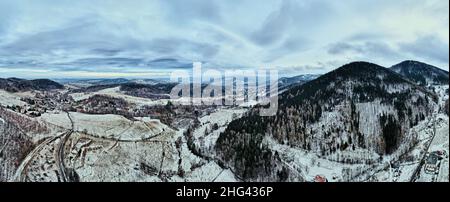 Kurvenreiche Straße durch mit Wald bedeckte Berge, Winterlandschaft mit kurviger Autobahn inmitten der Landschaft, Luftbild Stockfoto