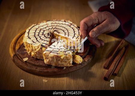 Eine Frau nimmt mit einem Löffel einen Esterhazy Mandel-Schokolade Kuchen auf einem Holzbrett liegend. Stockfoto