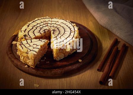 Tortenbrett mit geschnittenem Esterhazy-Kuchen mit Mandelschokolade, geschlagener Proteinmasse und Ölcreme mit Zusatz von Cognac auf einem Holztisch. Stockfoto