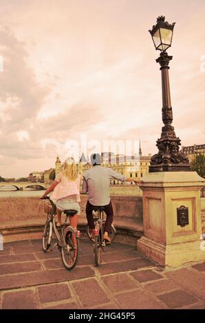 Ein Paar auf dem Fahrrad, das den Sonnenuntergang über Paris und der seine von Pont Neuf aus beobachtet, einer romantischen Szene in der französischen Stadt der Liebe Stockfoto