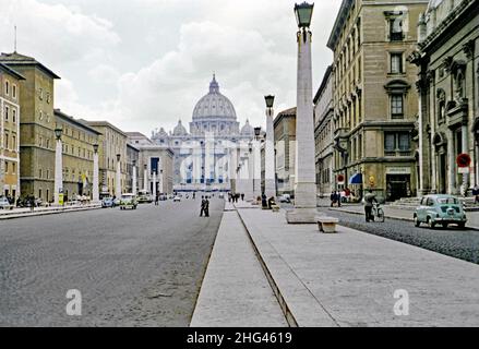 Die Via della Conciliazione (Straße der Schlichtung), Rom, Italien in c. 1960. Der Verkehr scheint in jenen Tagen ruhig zu sein. Die Straße verbindet Rom mit dem Petersplatz und der Basilika, Vatikanstadt (hinten). Die Straße wurde zwischen 1936 und 1950 gebaut. Der faschistische Diktator Benito Mussolini hat hier eine frühere Idee einer großen Durchgangsstraße wiederbelebt. Die Gebäude waren aus der Ausrichtung heraus, so dass die Illusion eines perfekt geraden Boulevards geschaffen wurde, wurden Fußgängerinseln ‘mit Reihen von Obelisken/Laternenpfosten gebaut. Dieses Bild stammt von einem alten Amateur 35mm Farbtransparenz – ein Vintage 1950/60s Foto. Stockfoto