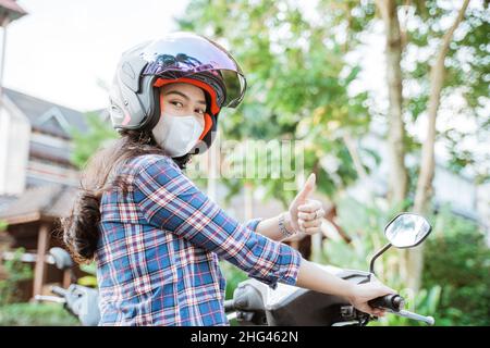 Frau trägt Helm und Maske mit Daumen nach oben während der Fahrt Stockfoto