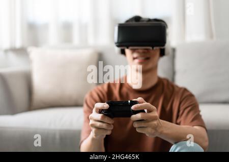 Technologiekonzept Ein Mann, der ein Virtual-Reality-Headset aufsetzt und ein schwarzes Konsolenspiel drückt, während er auf dem Boden sitzt. Stockfoto