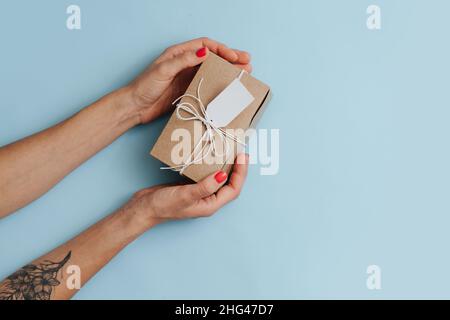 Draufsicht auf weibliche Hände, die einen mit Garn gebundenen Karton mit einem Anhänger auf einer blauen Oberfläche platzieren Stockfoto
