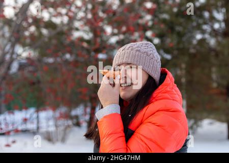 Weibliche Erwachsene, die Karotte als Nase auf dem Hinterhof des Hauses voller Schnee am Abend mit einem Spaziergang mit Bäumen und Eisenzaun im Hintergrund zu Gesicht. Eltern Stockfoto