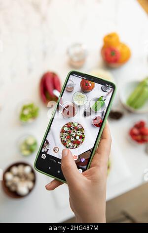 Frau fotografiert Pizza, die mit dem Handy gemacht wurde Stockfoto