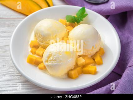 Drei Kugeln Mangoeis auf einem Teller auf hellem Hintergrund. Seitenansicht, Nahaufnahme. Erfrischendes Dessert. Stockfoto