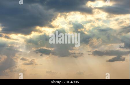 Die Sonnenstrahlen brechen bei Sonnenuntergang durch graue, dichte Wolken. Strahlendes Licht am Abendhimmel. Natürlicher Hintergrund. Stockfoto