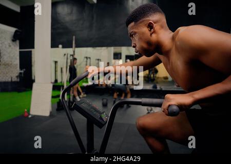 Afroamerikanischer Mann mit einem Crosstrainer während des Crosstrainings. Männlicher Athlet, der intensiv im Fitnessstudio trainiert. Hochwertige Fotos Stockfoto