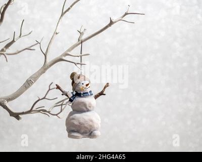Weihnachtsdekoration Schneemann hängt auf einem Baum Zweig auf silbernem Glitzer Hintergrund Stockfoto