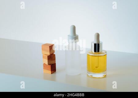 Gesichtsserum in matter Glasflasche und Gesichtsöl und gestapelten Zedernholzwürfeln auf weißem Hintergrund. Aufbau Ihrer Hautpflege Routine-Regime mit Peptiden A Stockfoto