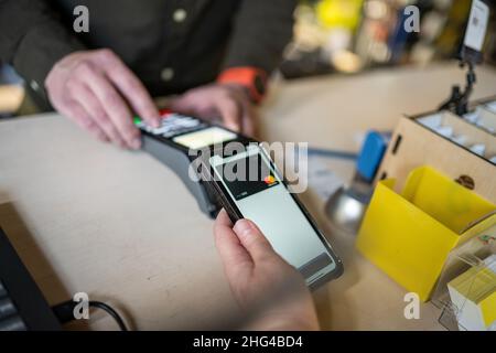 Frau zahlt per NFC-Technologie. Der Kunde zahlt per Mobiltelefon mit kontaktloser Technologie. Nahaufnahme Hände von mobilen Zahlung. Bezahlen Stockfoto