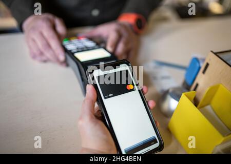 Nahaufnahme einer Frau, die über NFC bezahlt. Frau zahlt über Zahlungsterminal und Mobiltelefon. Kassierer Hand hält Kreditkarte Leser Maschine während Stockfoto