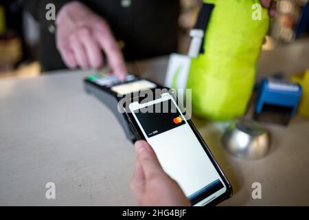 Nahaufnahme einer Frau, die über NFC bezahlt. Frau zahlt über Zahlungsterminal und Mobiltelefon. Kassierer Hand hält Kreditkarte Leser Maschine während Stockfoto