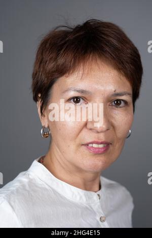 Nahaufnahme einer ziemlich reifen Frau mit kurzen braunen Haaren, die auf grauem Hintergrund isoliert auf die Kamera lächelt Stockfoto