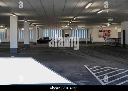 Die Schlussleuchten eines fahrenden Pkw in der Parkgarage eines Einkaufszentrums leuchten auf. Das Parkhaus ist leer, auf der rechten Seite befinden sich zahlreiche Parkplätze Stockfoto