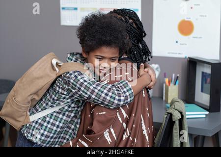 Glücklich anhänglich Schuljunge mit Rucksack geben Umarmung seiner Mutter, während immer bereit für die Schule am Morgen Stockfoto
