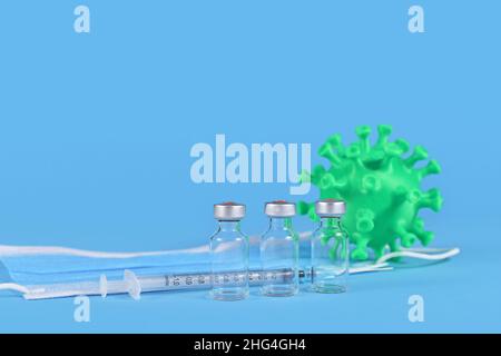 Auffrischungsimpfungskonzept mit 3 Fläschchen und Spritze, Gesichtsmaske und Corona-Virus-Modell auf blauem Hintergrund mit Kopierraum Stockfoto