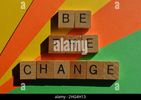 Be the Change, Wörter in hölzernen Buchstaben auf mehrfarbigem Hintergrund isoliert Stockfoto