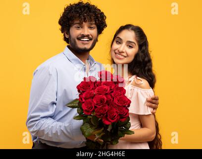 Porträt eines liebenden indischen Paares mit Blumenstrauß, lächelnd und mit Blick auf die Kamera, um den Valentinstag zu feiern Stockfoto
