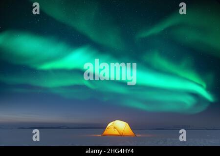 Gelbes Zelt von innen beleuchtet vor dem Hintergrund eines unglaublichen Sternenhimmels mit Aurora Borealis. Tolle Nachtlandschaft. Nordlichter im Winterfeld Stockfoto