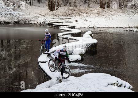 Radfahren im Winter. Die Radfahrer im Mountainbike-Getriebe überqueren den künstlichen Wasserfall auf dem Fluss Swisloch im Winter. Minsk. Weißrussland Stockfoto