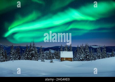 Fantastische Winterlandschaft mit Holzhaus in verschneiten Bergen und nordischem Licht am Nachthimmel. Weihnachtsferien und Winterurlaub Konzept Stockfoto