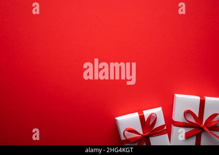 Kreatives Postkarten-Design am Valentinstag mit weißer Geschenkbox und roter Schleife auf rotem Papierhintergrund. Valentinstag und Liebeskonzept Stockfoto