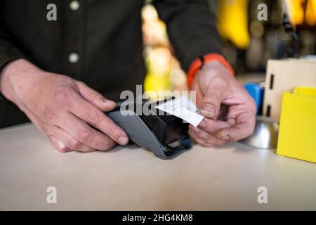 Der Verkäufer hält das Zahlungsterminal, während er den Beleg für den Abschluss des Kaufs hält. Nahaufnahme der Hände. Konzept von NFC, Geschäfts- und Bankgeschäften Stockfoto