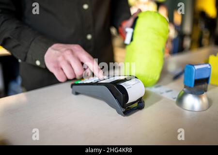 Der Verkäufer hält das Zahlungsterminal, während er den Beleg für den Abschluss des Kaufs hält. Nahaufnahme der Hände. Konzept von NFC, Geschäfts- und Bankgeschäften Stockfoto