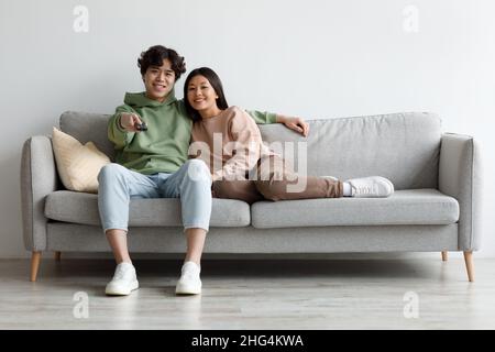 Millennial Asian paar beim Film, mit Fernbedienung, Kuscheln auf der Couch zu Hause, kopieren Raum Stockfoto