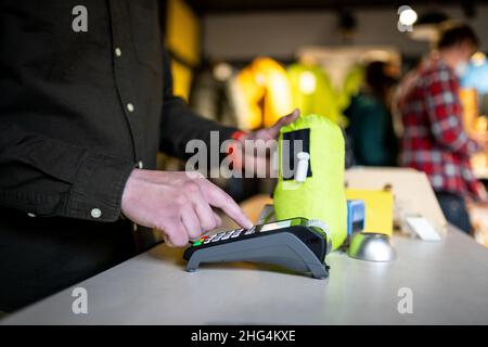 Der Mann hält das Zahlungsterminal, während er den Beleg für den Abschluss eines Kaufs hält. Nahaufnahme der Hände und Seitenansicht. Konzept von NFC, Business und Banking Stockfoto