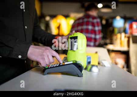 Der Verkäufer hält das Zahlungsterminal, während er den Beleg für den Abschluss des Kaufs hält. Nahaufnahme der Hände. Konzept von NFC, Geschäfts- und Bankgeschäften Stockfoto