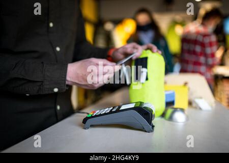 Der Mann hält das Zahlungsterminal, während er den Beleg für den Abschluss eines Kaufs hält. Nahaufnahme der Hände und Seitenansicht. Konzept von NFC, Business und Banking Stockfoto