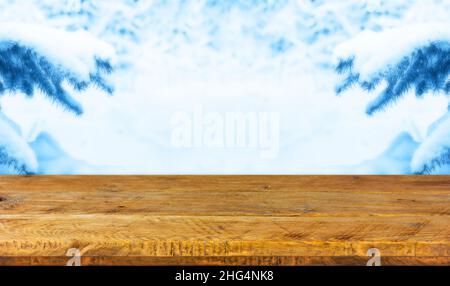 Ein Holzbrett, eine leere Tischplatte und ein verschwommener Hintergrund mit Ästen eines Weihnachtsbaums im Schnee. Modell zur Präsentation des Produkts. Stockfoto