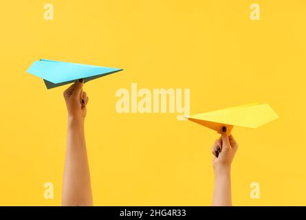 Die Hände einer Frau halten bunte Papierflugzeuge auf gelbem Hintergrund. Wettbewerbskonzept. Stockfoto