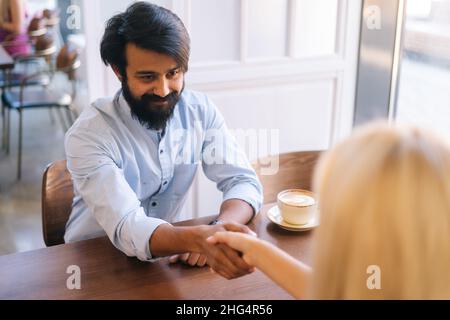 Nahaufnahme von oben, von zwei männlichen und weiblichen Geschäftspartnern, die im Café die Hände über den Kaffee schüttelten. Stockfoto