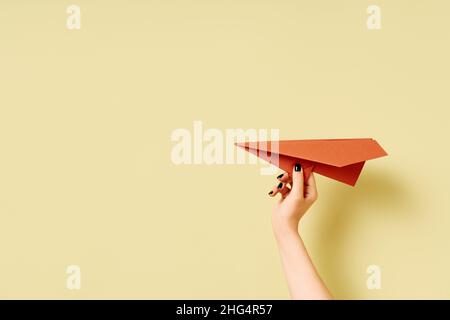 Eine Frauenhand hält ein Flugzeug aus Terrakotta-Papier auf olivgrünem Hintergrund mit Kopierraum Stockfoto