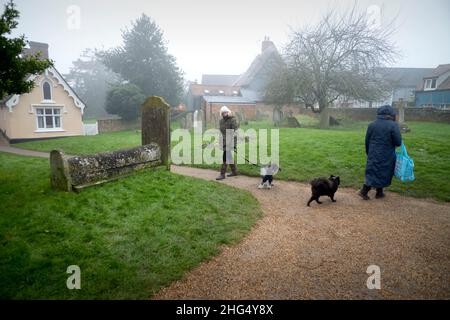 Thaxted, Großbritannien. 18th Januar 2022. Thaxted Essex England UK an einem Misty Winters Day 18. Januar 2022 Ein ruhiges Zwischenspiel für zwei Hundewanderer in einem ländlichen Kirchhof in Misty Thaxted in North West Essex. Foto: BRIAN HARRIS/Alamy Live News Stockfoto