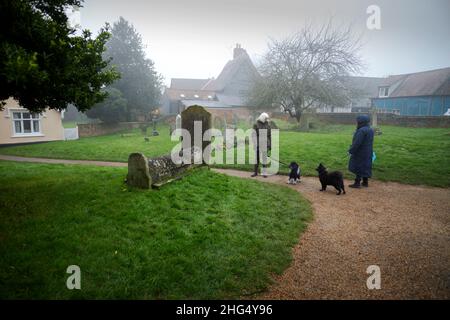 Thaxted, Großbritannien. 18th Januar 2022. Thaxted Essex England UK an einem Misty Winters Day 18. Januar 2022 Ein ruhiges Zwischenspiel für zwei Hundewanderer in einem ländlichen Kirchhof in Misty Thaxted in North West Essex. Foto: BRIAN HARRIS/Alamy Live News Stockfoto