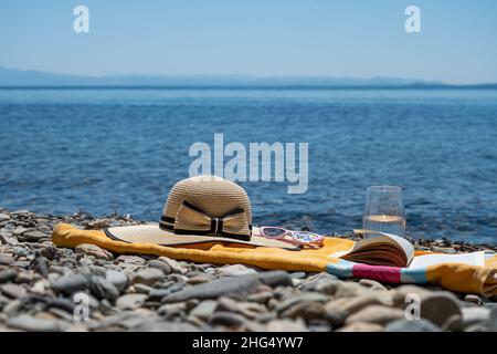 Sommerferienkonzept am Meer mit Handtuch, Hut und Buch, Freizeitaktivitäten am Strand im Urlaub Stockfoto