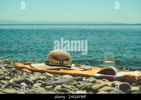 Sommerferienkonzept am Meer mit Handtuch, Hut und Buch, Freizeitaktivitäten am Strand im Urlaub Stockfoto